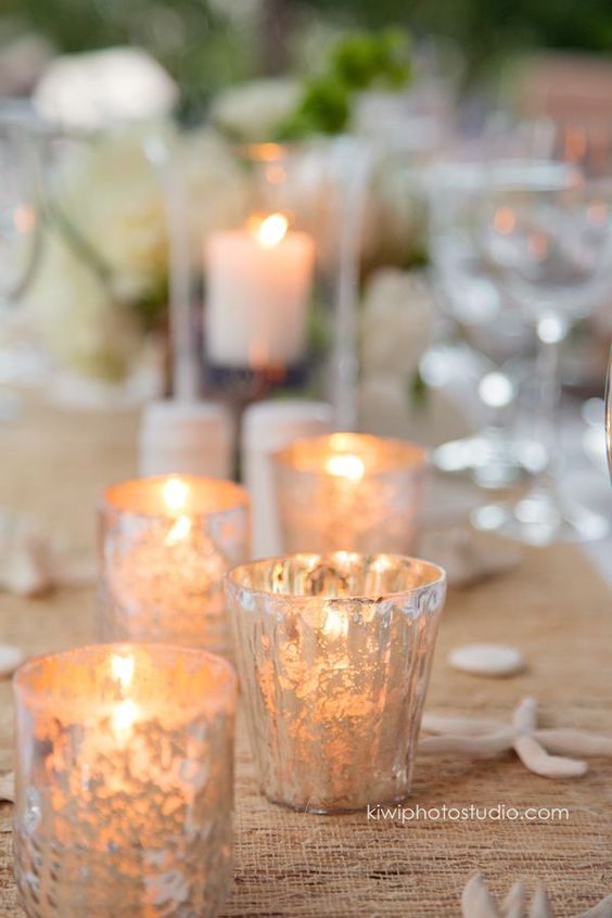 Adorable votives, shells and white flowers to decorate this beach wedding reception tables. Photography: kiwiphotostudio.