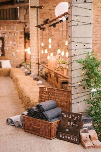 We love the rustic meets industrial decor vibe. Bales of hay, exposed brick and hanging Edison bulbs. Blankets in a basket favors make loving winter wedding ideas.