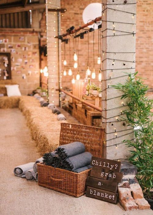 We love the rustic meets industrial decor vibe. Bales of hay, exposed brick and hanging Edison bulbs. Blankets in a basket favors make loving winter wedding ideas.